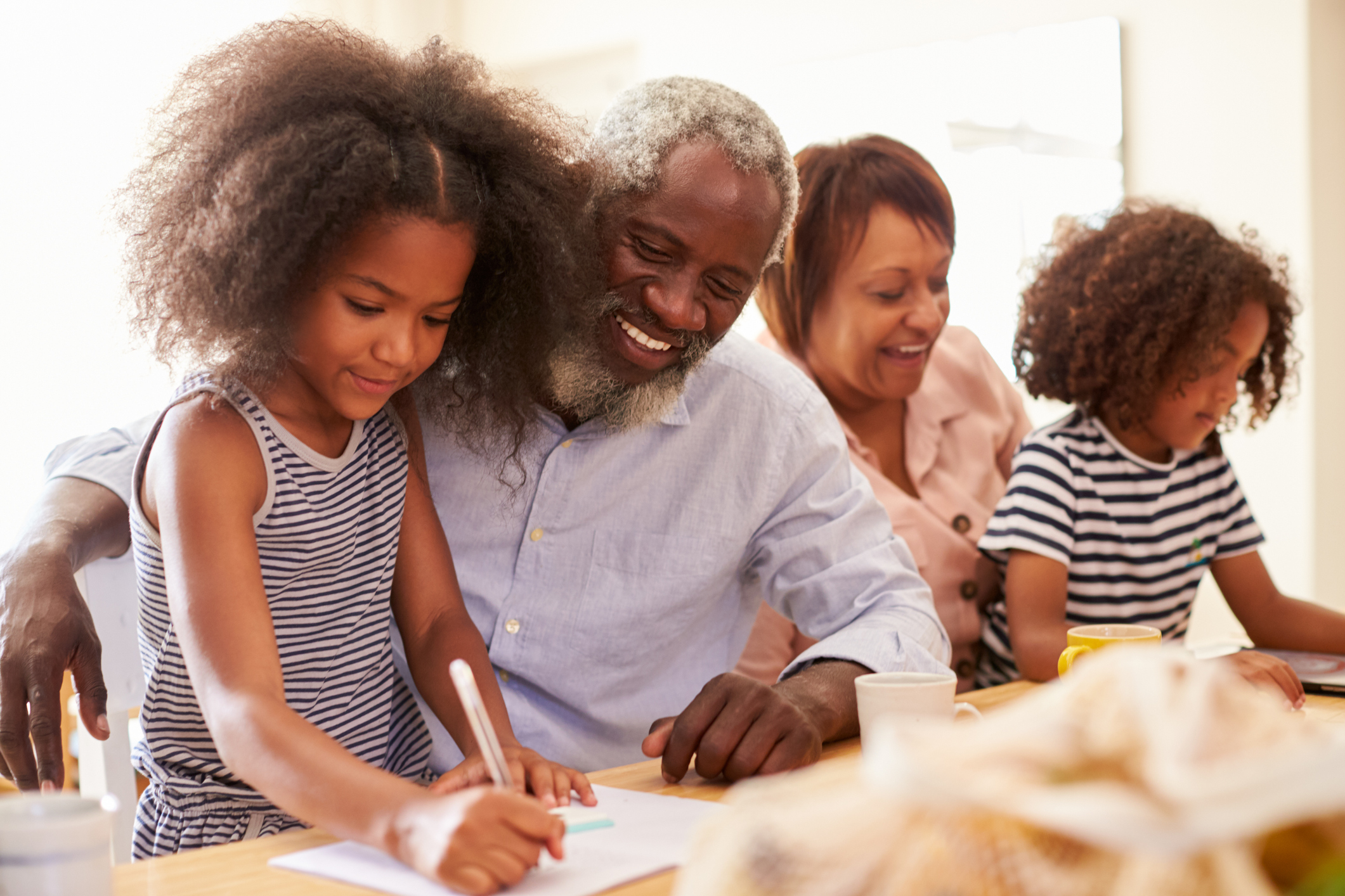 A grandfather and grandmother sitting at a kitchen table drawing with their two grandchildren